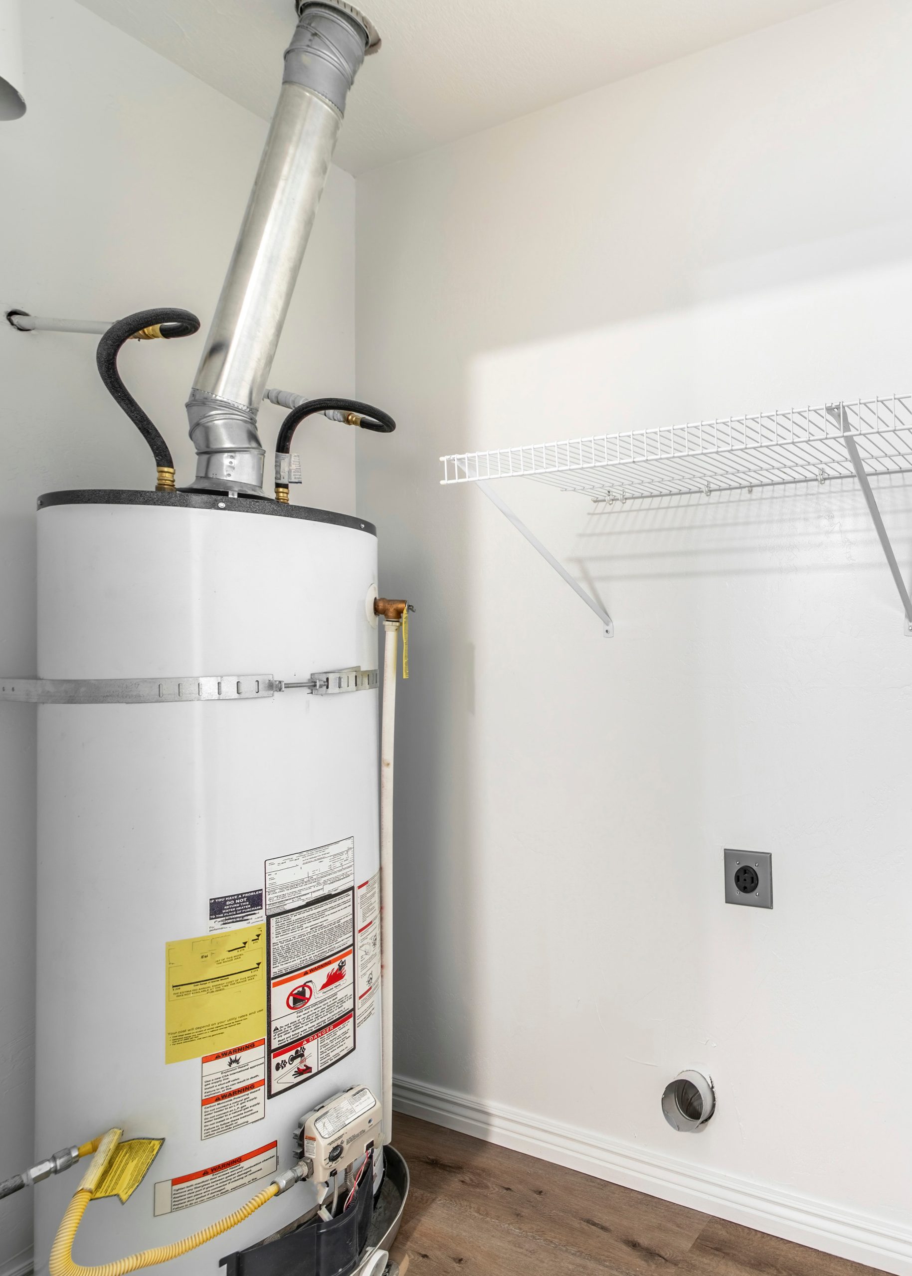 vertical empty white laundry room with water heater tank and wall mounted wire shelf